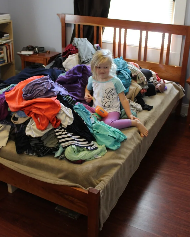 little girl in a pile of clothes in a bed