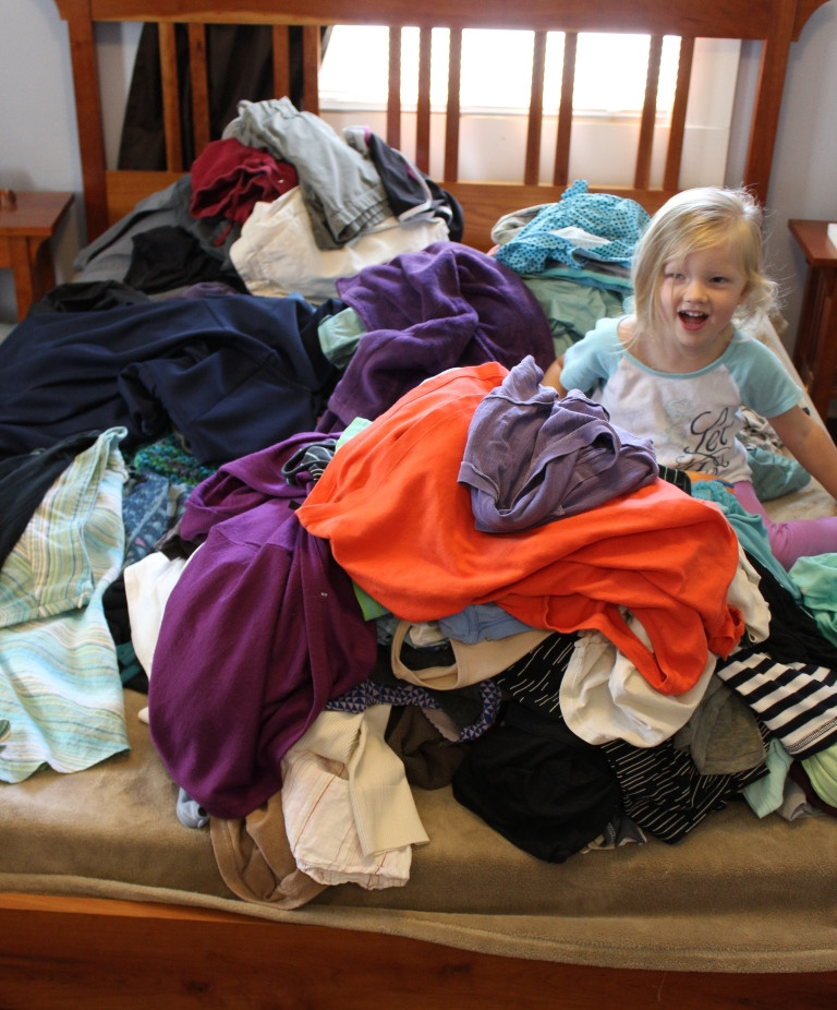little girl in a pile of clothes on a bed 
