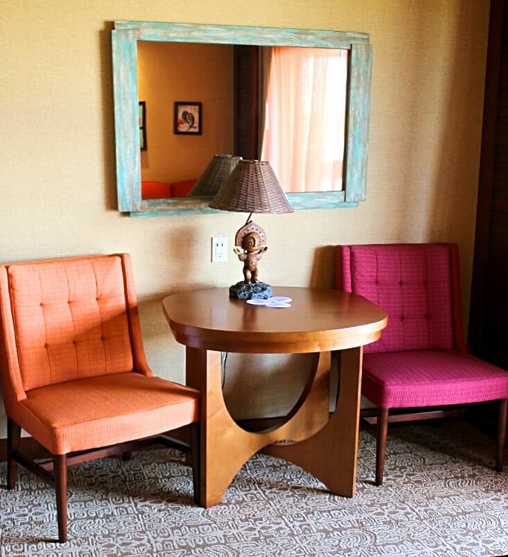 sitting area with orance and pink chair, brown table and lamp, and blue mirror