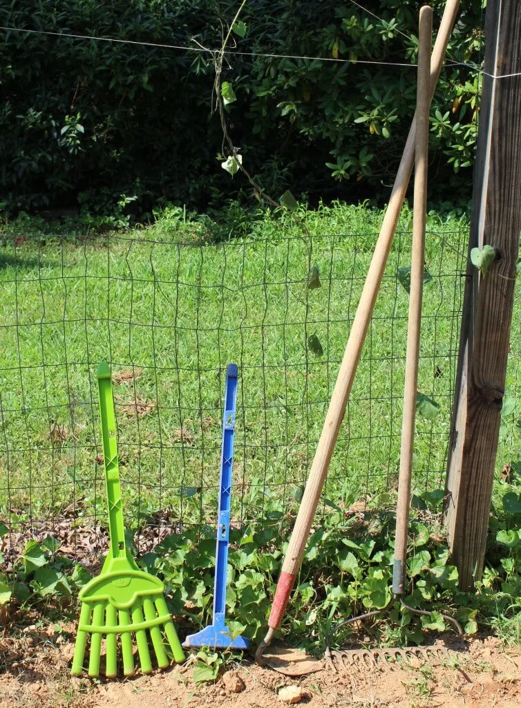 child garden tools next to regular gardening tools leaning on a fence