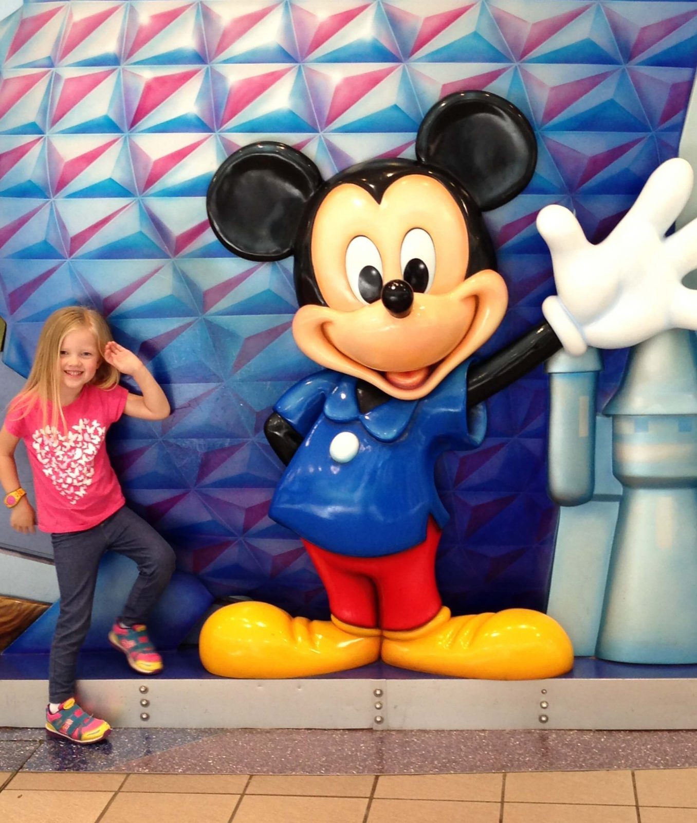 little girl posing next to mickey mouse statue at airport