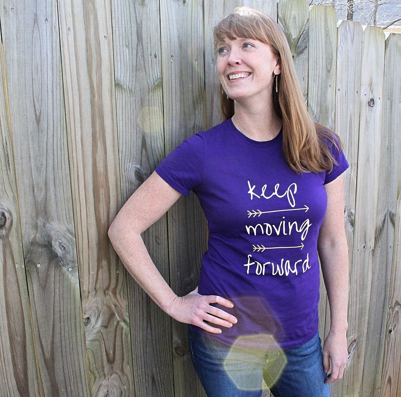 Model posing in front of a wood fence in the blue keep moving forward tshirt