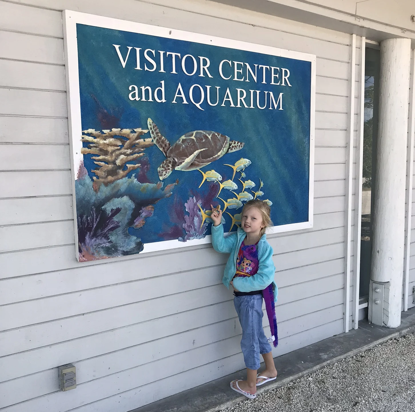 little girl in front of the visitor center and aquarium sign