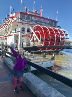 girl standing and smiling next to water and ferry boat