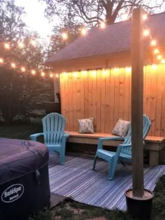 Backyard with 2 blue adirondack chairs, wooden bench and white hanging lights