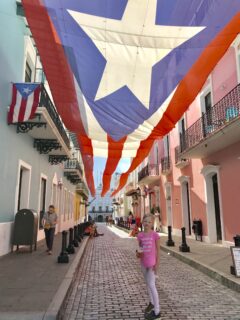 girl standing on brick street with long Puerto Rico flag hanging above